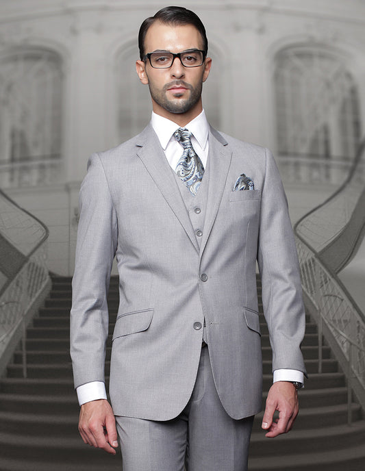 A man dressed in Statement Clothing's stylish TZ-100BG-GRAY suit, featuring pleated pants, complemented by a paisley tie, stands confidently in front of a grand staircase.