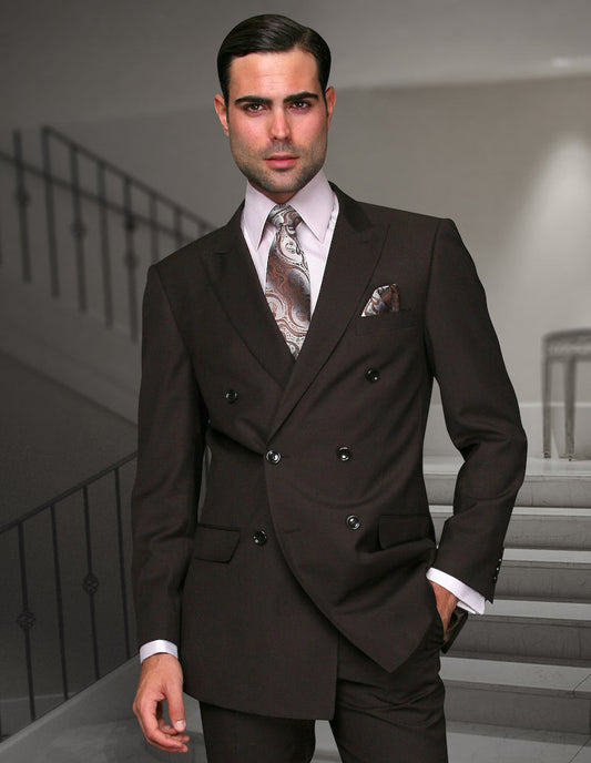 A man wearing a dark brown, regular-fit double-breasted suit by Statement Clothing (TZD-100-BROWN), paired with pleated pants, a patterned tie, and a pocket square, stands indoors on a staircase.