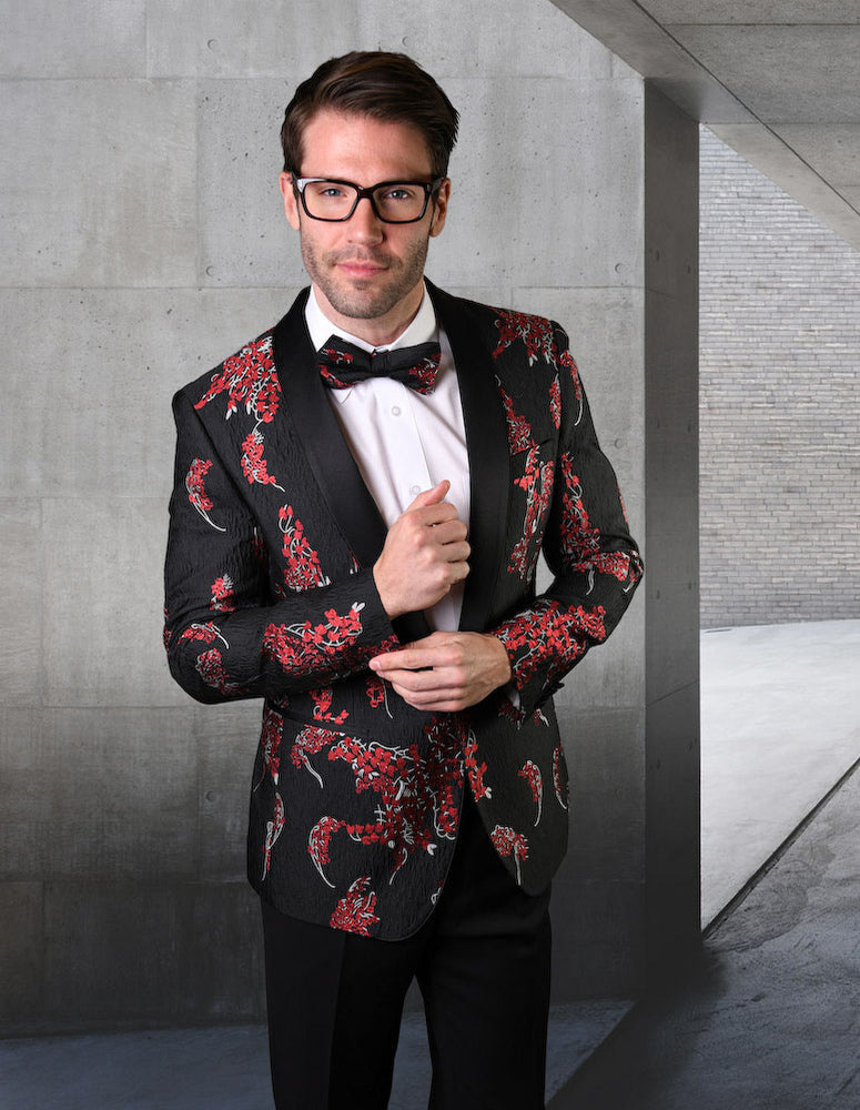 A man wearing the tailored STATEMENT CLOTHING | VJ-121-BLACK suit with a floral pattern and coordinating bow tie stands in a concrete hallway, looking at the camera.