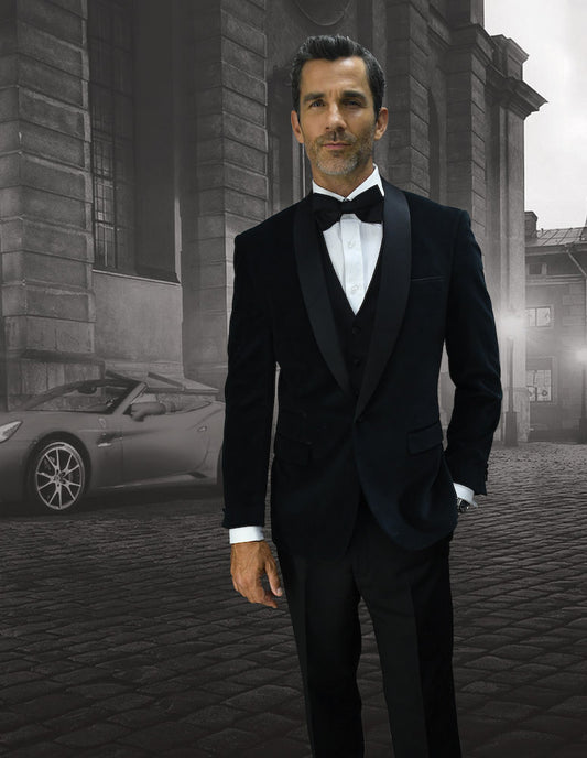 A man dressed in Statement Clothing's VL-100-BLACK tuxedo with a tailored fit stands on a cobblestone street, exuding elegance with a bow tie, as a convertible car gleams in the background.