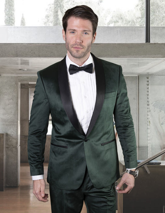 A man wearing the STATEMENT CLOTHING | VL-100-HUNTER suit from Statement Clothing, featuring a tailored fit in hunter green velvet with a shawl lapel and complemented by a black bow tie, stands indoors.