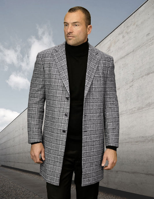 A man wearing the STATEMENT CLOTHING | WJ-103-BLACK, a modern-fit plaid jacket crafted from wool and cashmere by Statement Clothing, stands outdoors against a cloudy sky and concrete wall backdrop, exuding timeless style with his black turtleneck.