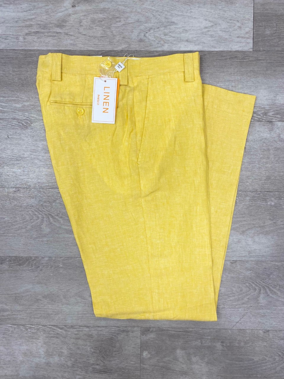 The Inserch Premium Linen Flat Front Pants P3116 in Yellow are stylishly displayed on a gray wooden floor, showcasing a sophisticated look with their single button detail and "Linen" tag. Ideal for warm weather, these casual pants from the brand Inserch seamlessly combine comfort and style.