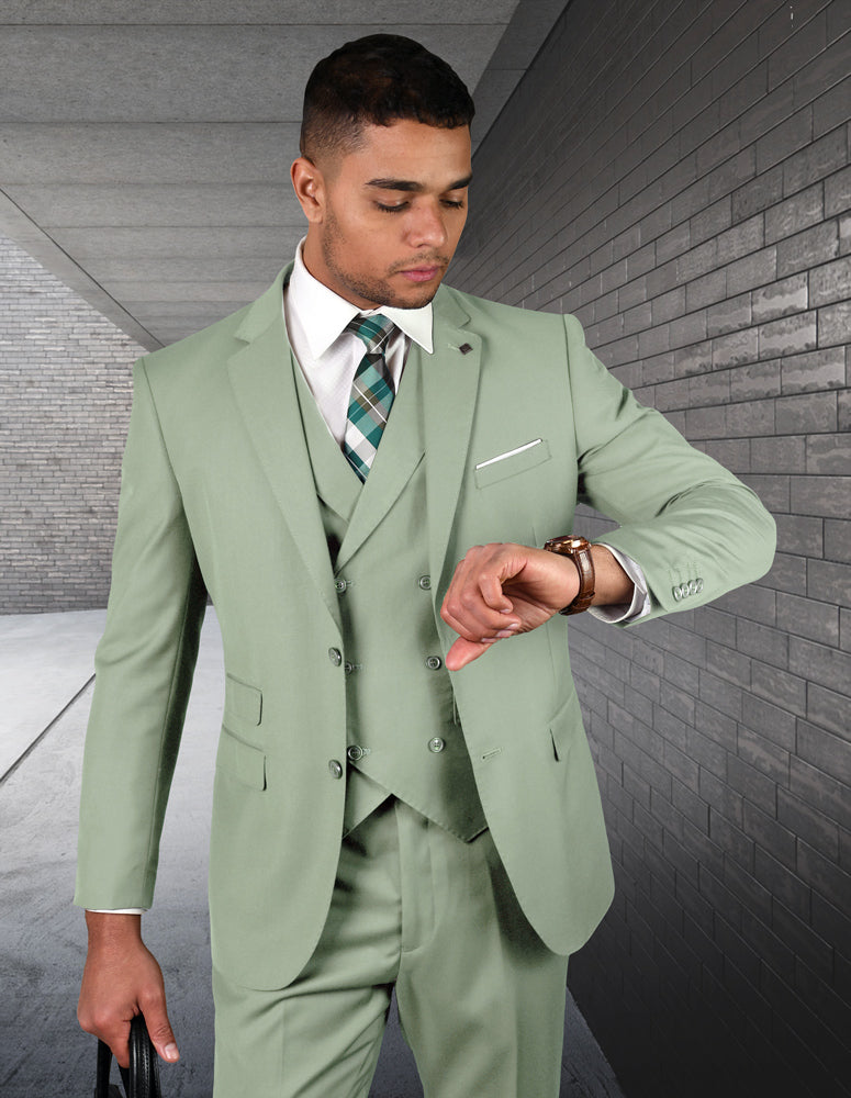 A man wearing the STATEMENT CLOTHING | ZARGALA-APPLEGREEN suit from Statement Clothing, paired with a patterned tie, checks his watch while standing in a corridor with brick walls.