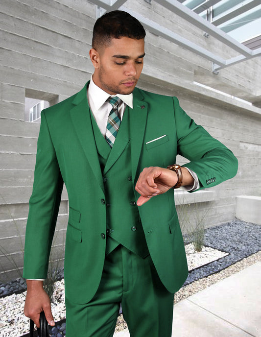 A man in the ZARGALA-KELLYGREEN suit from Statement Clothing, complete with a tie, checks his watch in a contemporary building setting. The elegant Italian Wool fabric of the suit accentuates his sleek, modern fit.