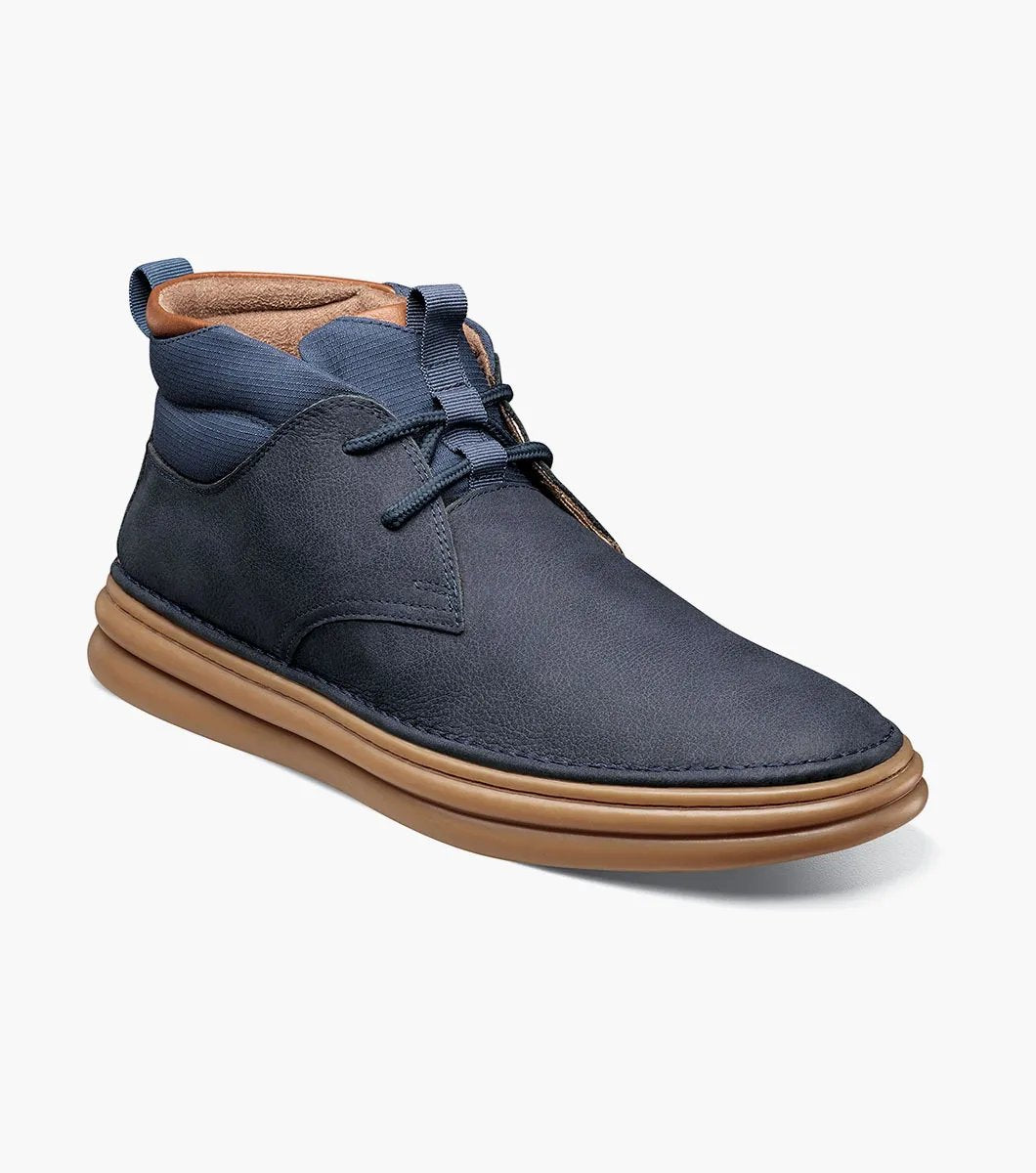 The Stacy Adams DELSON Plain Toe Chukka Boot in Navy showcases a leather upper paired with brown soles and laces, featuring anatomical arch support, set against a white background.