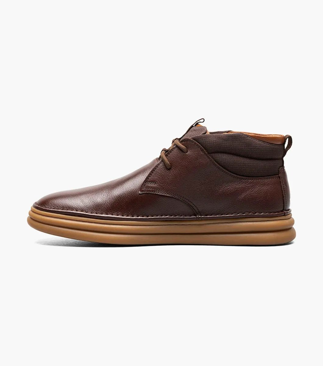 The Stacy Adams DELSON Plain Toe Chukka Boot in Chocolate, style number 25556-202, features a brown leather design with a rounded toe, lace-up front, and a cushioned brown sole with anatomical arch support, all presented against a white background.