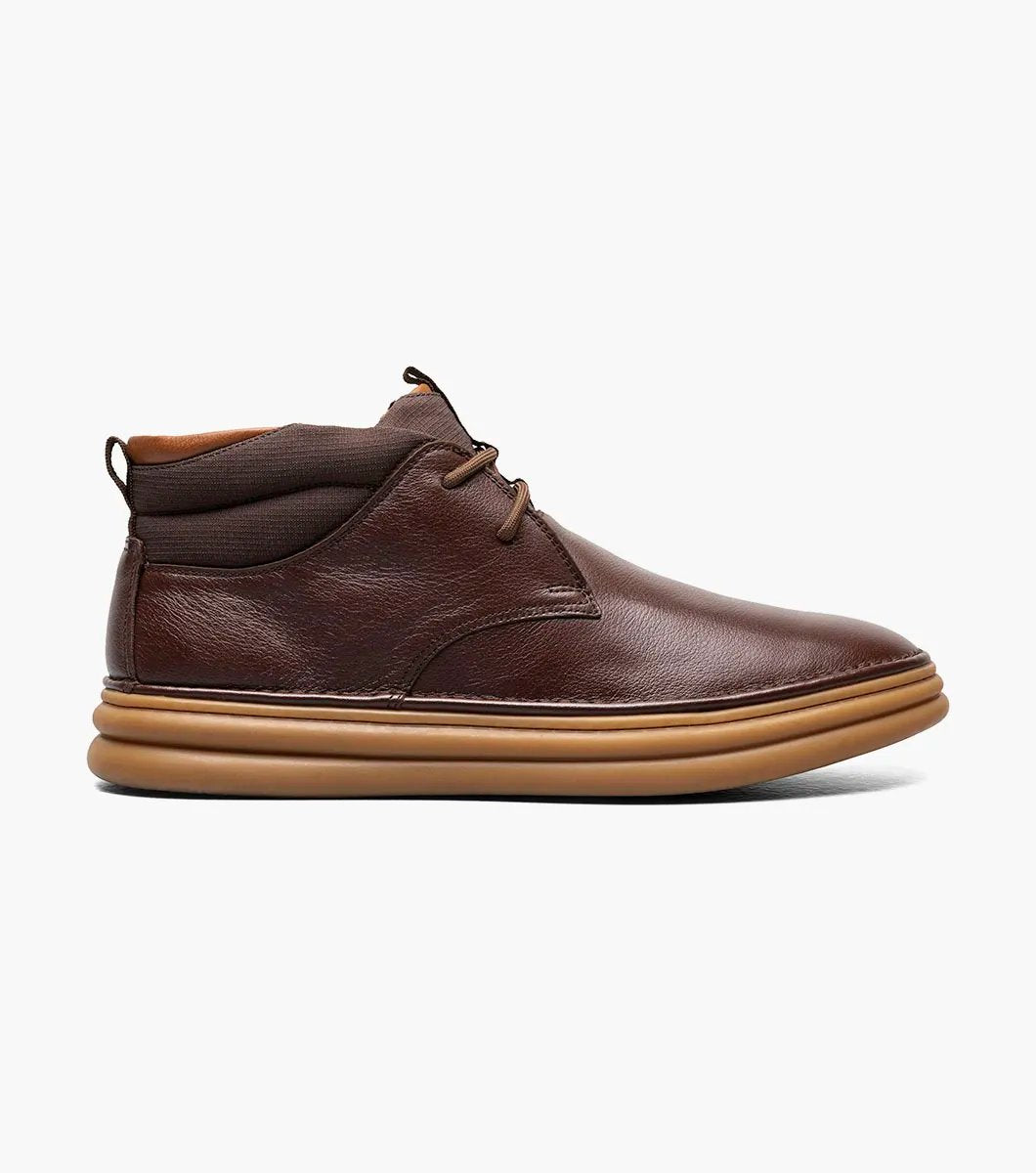 The Stacy Adams DELSON Plain Toe Chukka Boot in Chocolate, style number 25556-202, features a brown leather design with a rounded toe, lace-up front, and a cushioned brown sole with anatomical arch support, all presented against a white background.