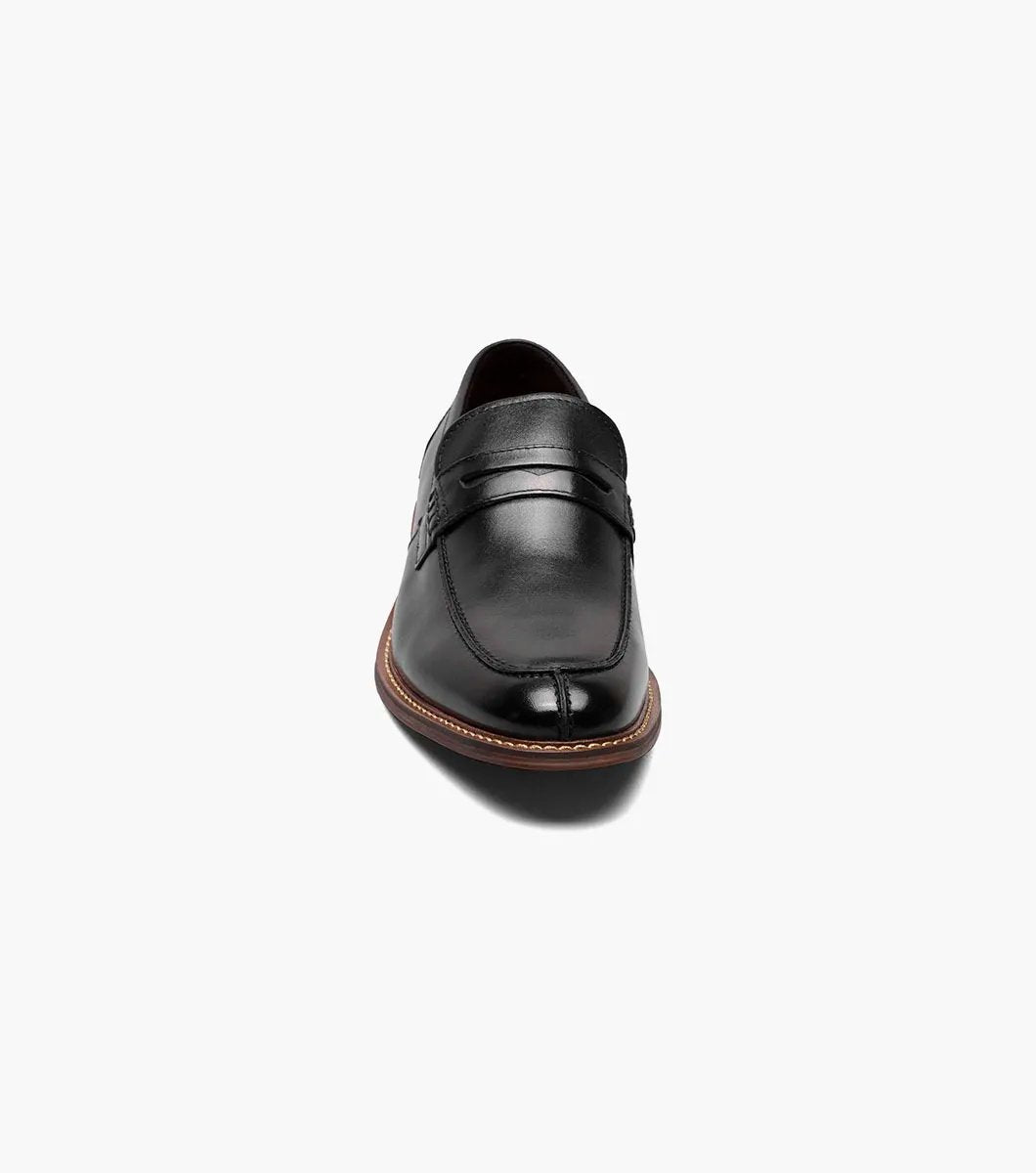 The Stacy Adams MARLOWE Algonquin Moc Toe Penny Slip On in black, featuring a refined leather upper and a contrasting brown sole, is displayed against a plain background.