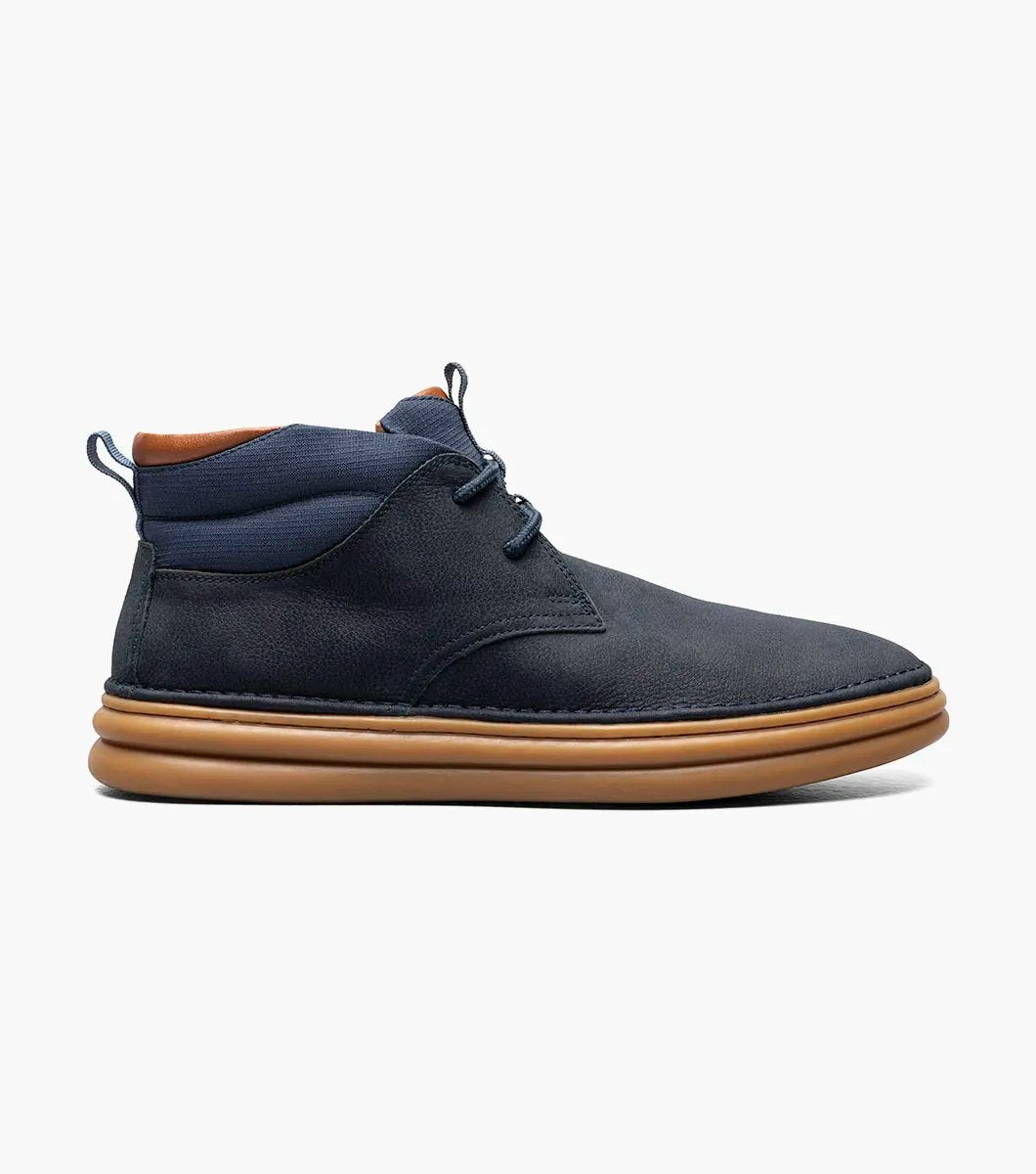 The Stacy Adams DELSON Plain Toe Chukka Boot in Navy showcases a leather upper paired with brown soles and laces, featuring anatomical arch support, set against a white background.