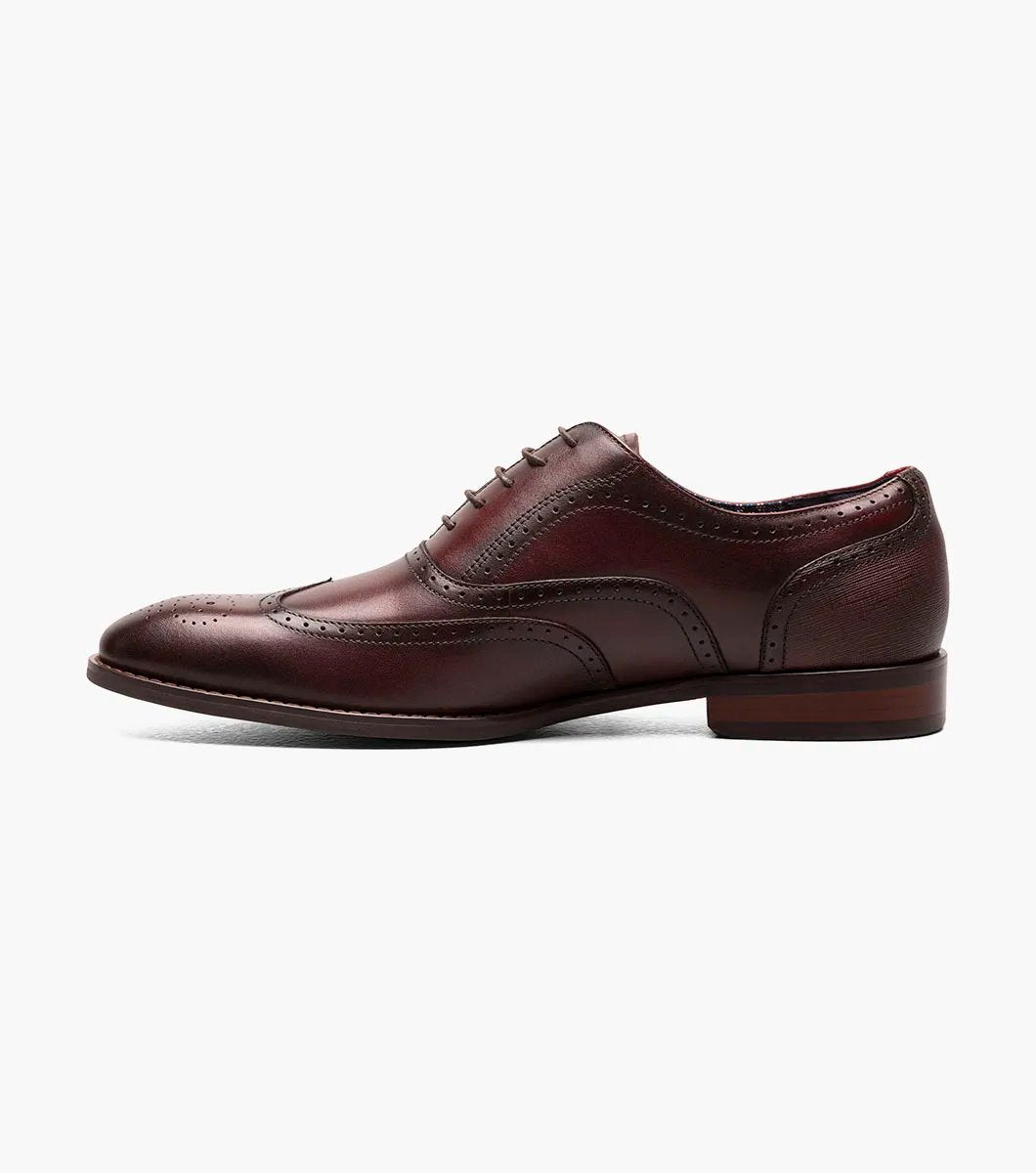 The Stacy Adams KAINE Wingtip Oxford in Burgundy, model number 25569-601, showcases a leather upper with decorative perforations and a classic wingtip design. This brogue dress shoe features a low heel and is photographed on a white background, highlighting its elegance and anatomical arch support for added comfort.