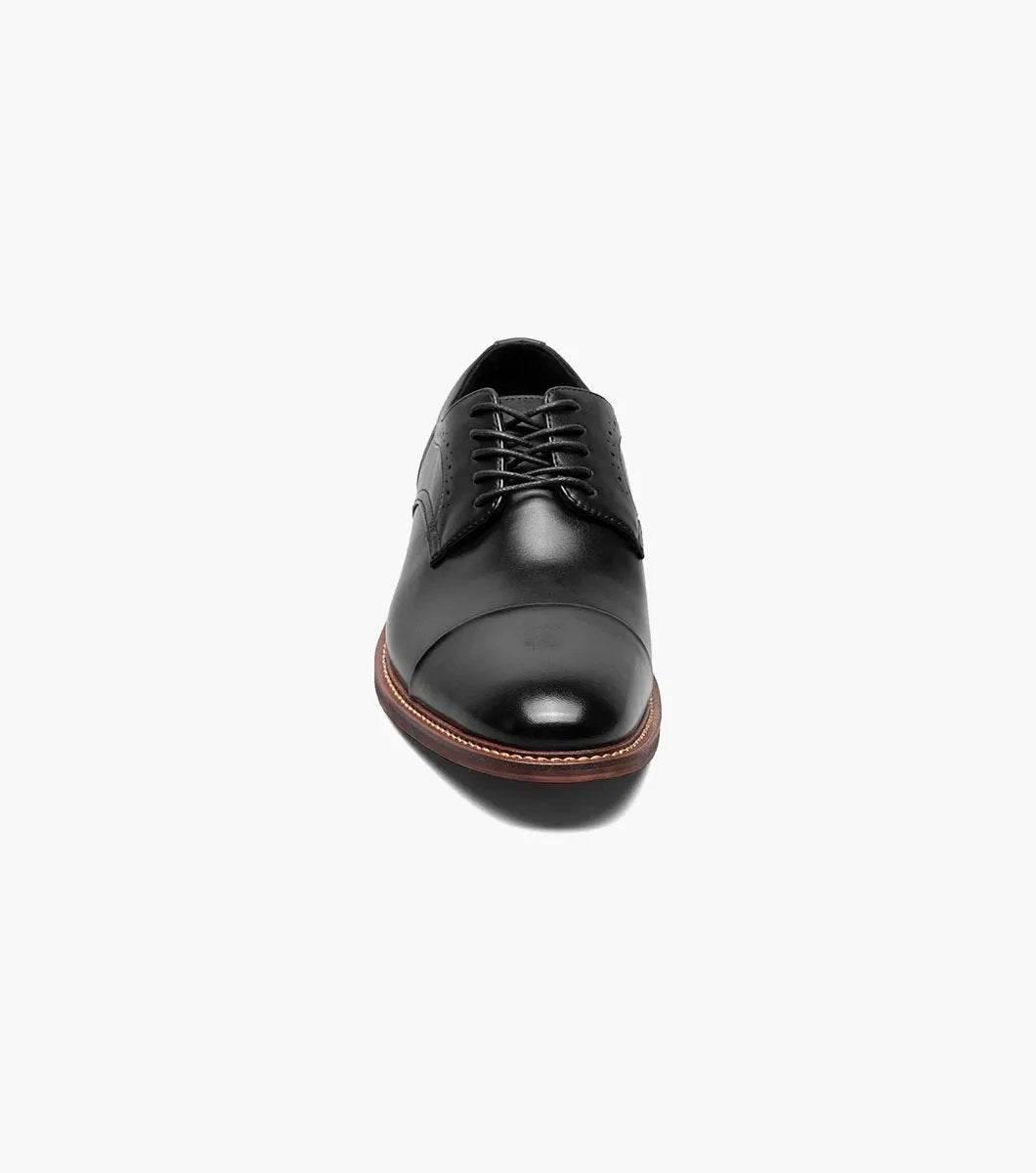 The Stacy Adams - MADDOX Cap Toe Oxford shoe features a black smooth leather finish with a polished appearance, complemented by a brown sole, intricate decorative stitching, and anatomical arch support.