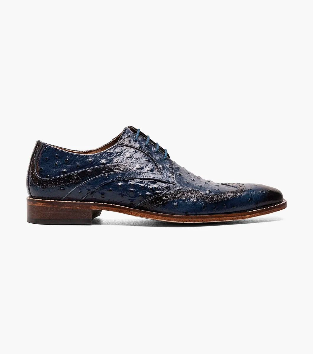 The Stacy Adams GENNARO Wingtip Oxford in blue, style number 25537-400, showcases intricate brogue detailing and comes with a contrasting brown sole. Set against a plain white background, it delivers unparalleled comfort through its anatomical arch support while melding elegance with functionality.