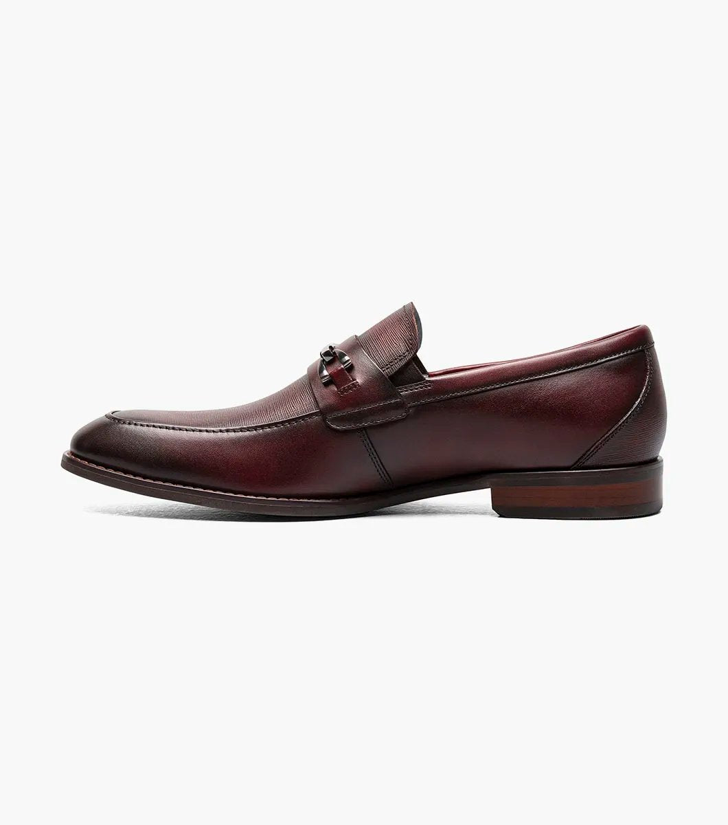 The Stacy Adams KAYLOR Moc Toe Bit Slip On in Burgundy, product number 25572-601, features a metal buckle detail, leather upper, low heel, and dark sole set against a plain white background.