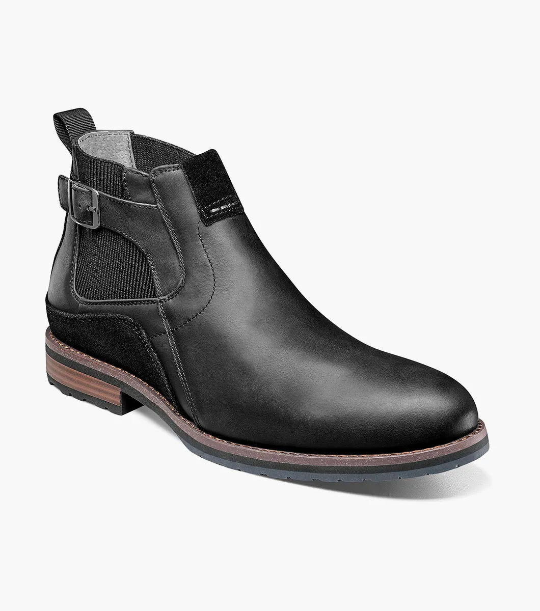 The Stacy Adams OSKAR Plain Toe Chelsea Boot in Black Waxy features a black leather design with a side buckle, an elastic gusset, and a brown sole. Its stylish mixed material upper adds an extra touch of flair.