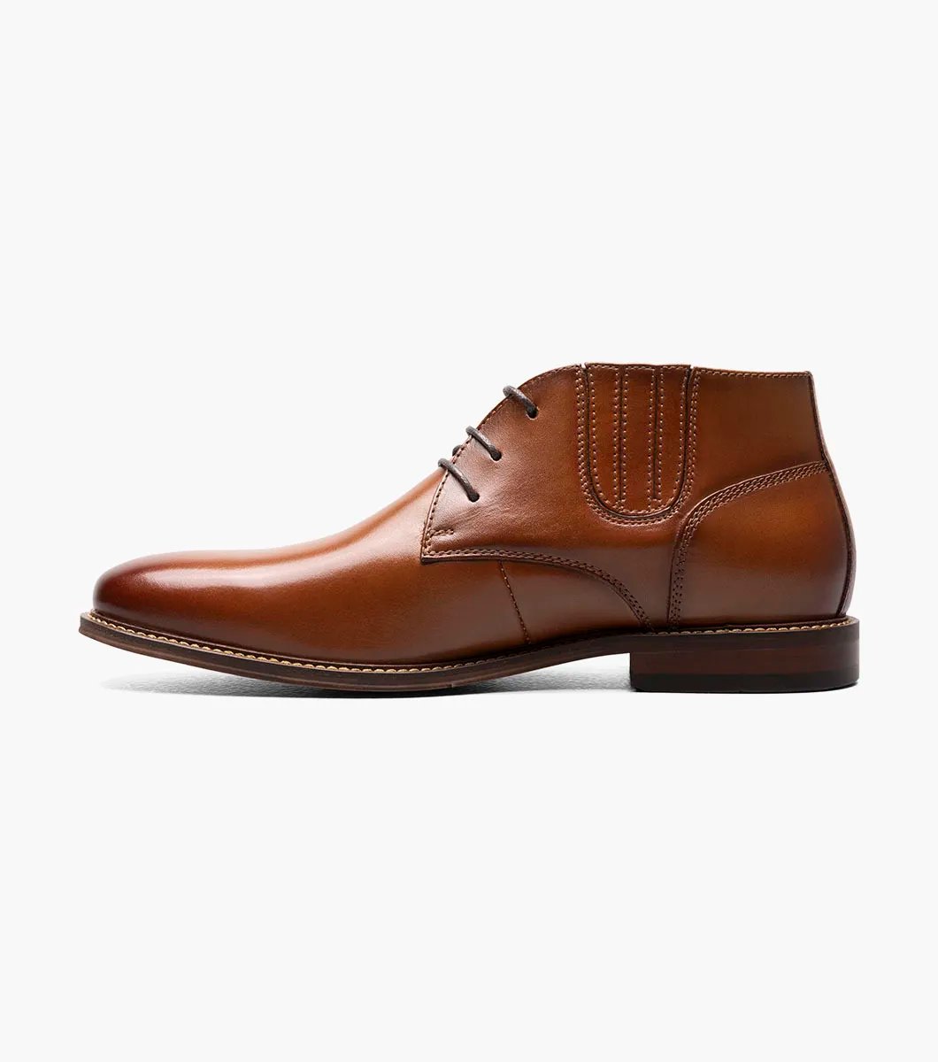 The Stacy Adams Maxwell Plain Toe Chukka Boot in Cognac features a sophisticated leather design with three eyelets, detailed stitching, and a versatile low heel, making it ideal for both dressy and casual events.