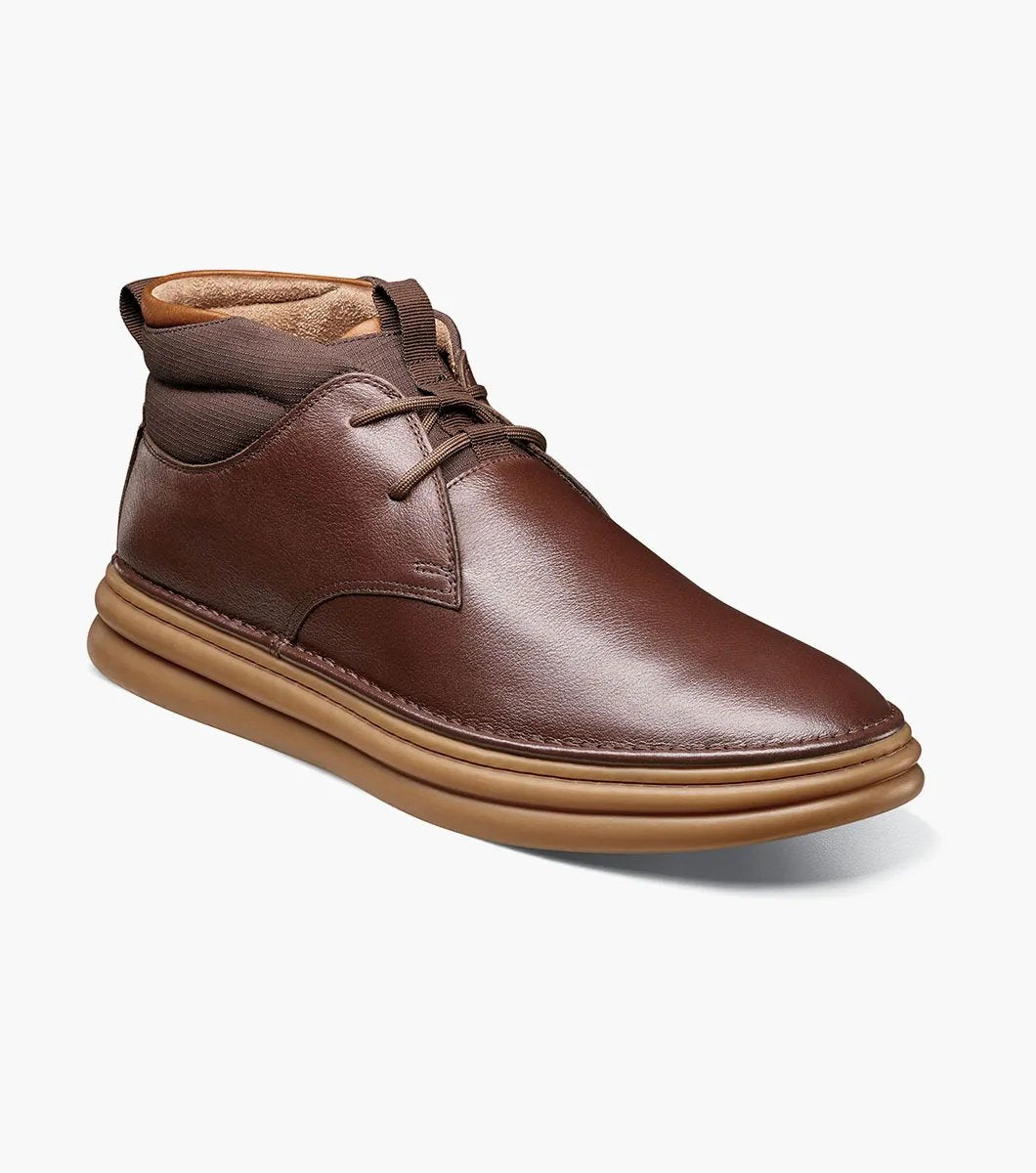 The Stacy Adams DELSON Plain Toe Chukka Boot in Chocolate, style number 25556-202, features a brown leather design with a rounded toe, lace-up front, and a cushioned brown sole with anatomical arch support, all presented against a white background.