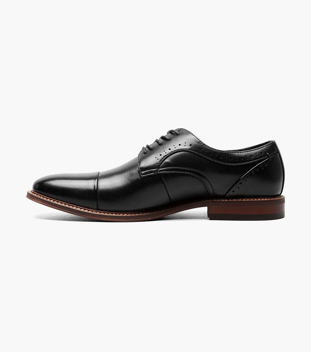 The Stacy Adams - MADDOX Cap Toe Oxford shoe features a black smooth leather finish with a polished appearance, complemented by a brown sole, intricate decorative stitching, and anatomical arch support.