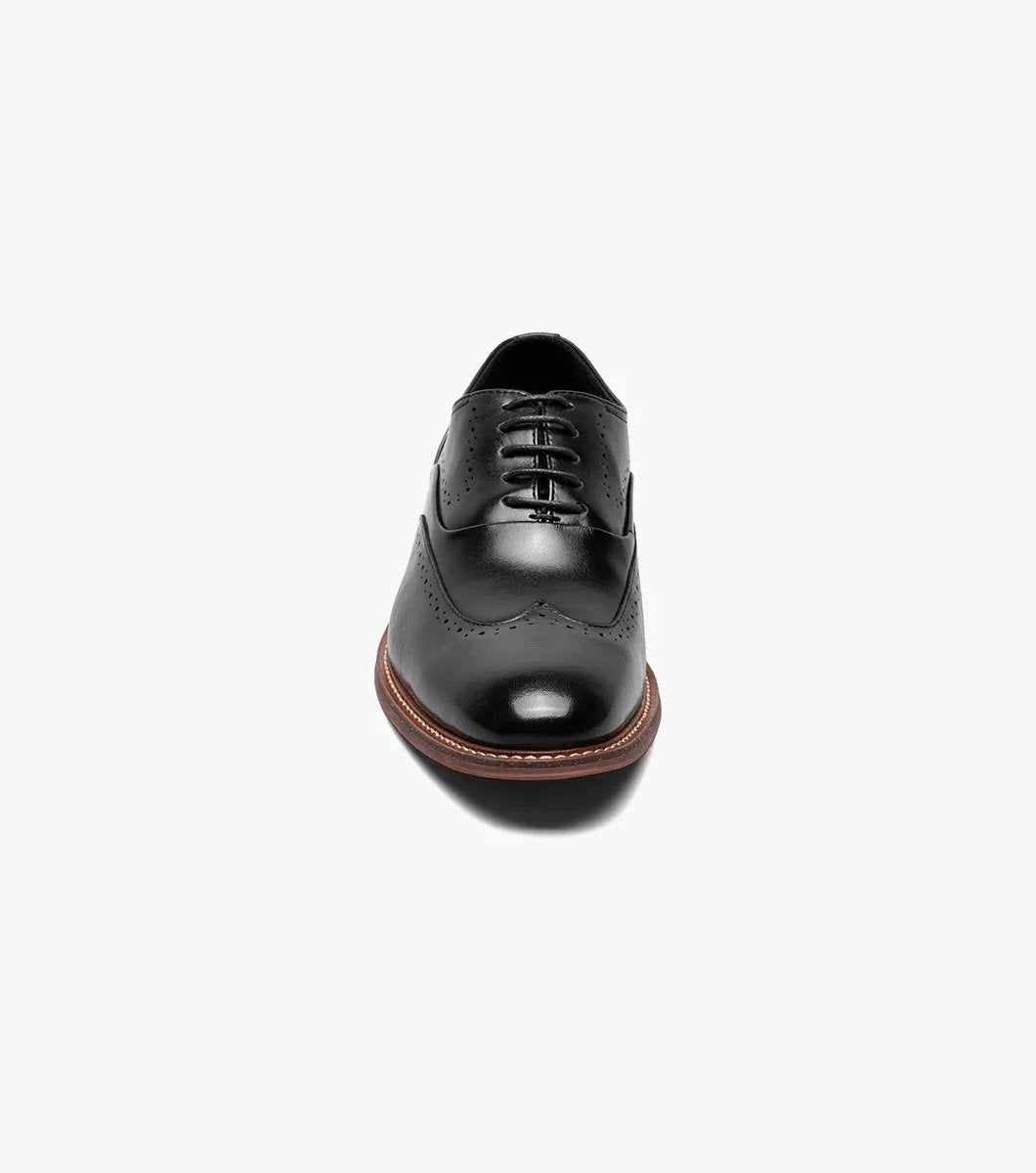 The Stacy Adams MACARTHUR Wingtip Oxford in Black Smooth, featuring decorative perforations and a sophisticated wingtip design with a brown heel and lace-up closure, is elegantly displayed on a white background.