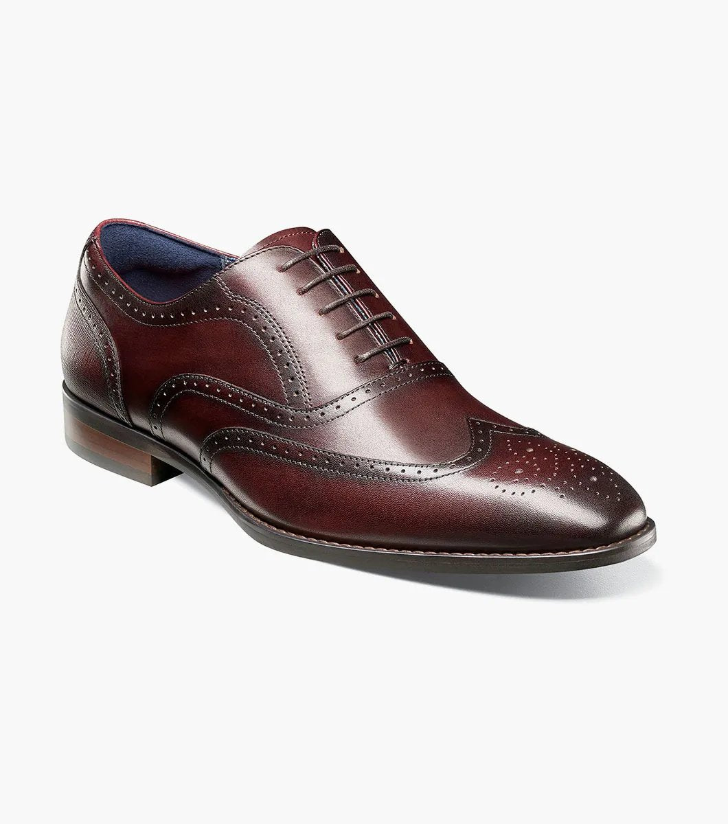 The Stacy Adams KAINE Wingtip Oxford in Burgundy, model number 25569-601, showcases a leather upper with decorative perforations and a classic wingtip design. This brogue dress shoe features a low heel and is photographed on a white background, highlighting its elegance and anatomical arch support for added comfort.