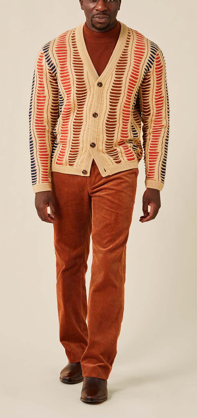 A person wearing a beige, blue, and red patterned cardigan over a brown shirt, paired with Inserch Cotton Flat Front Corduroy Pants P3103-05 Caramel from the brand Inserch and brown shoes, stands against a plain background.