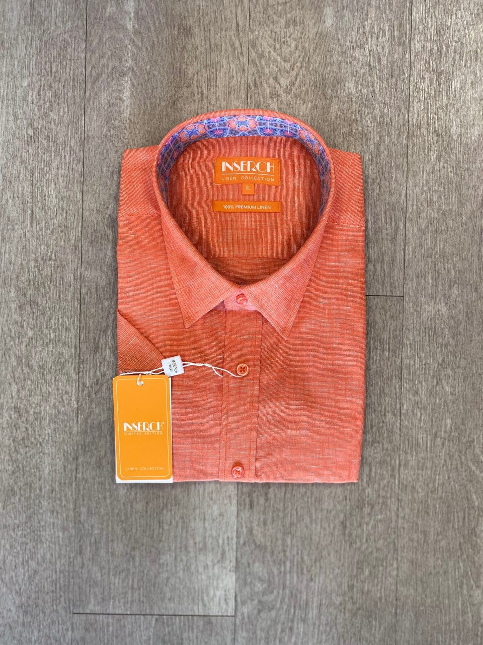 An orange short-sleeve shirt from Inserch, made with premium linen yarn dye, neatly folded on a wooden floor with a tag attached.