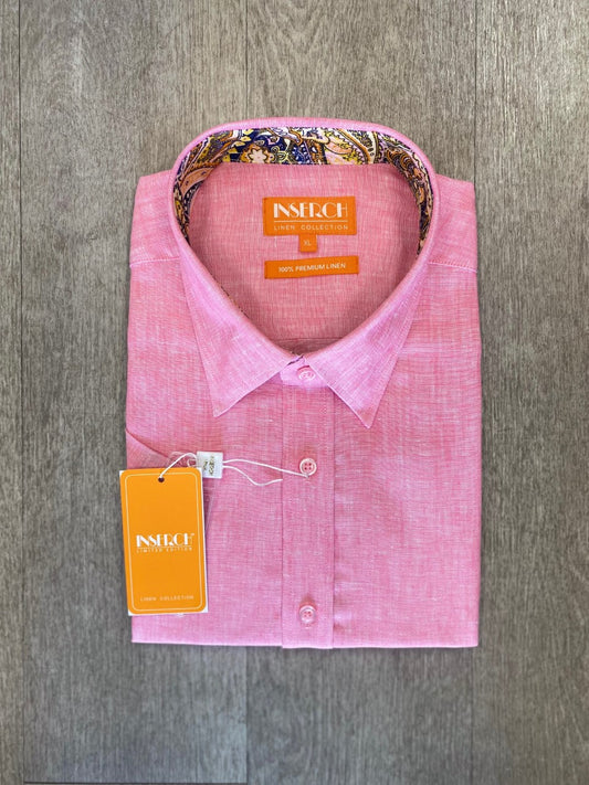 The Premium Linen Yarn Dye Short Sleeve Shirt in pink by Inserch, featuring a patterned inner collar, brand label, and an attached orange tag, is neatly folded and placed on a wooden surface.